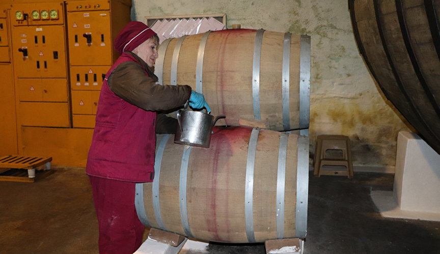 Сотрудник подливает вино в бочку в винном подвале завода марочных вин INKERMAN